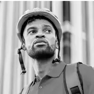 A focused construction worker in black and white, wearing a safety helmet and looking into the distance, reflecting determination, professionalism, and dedication to his craft against an urban backdrop.